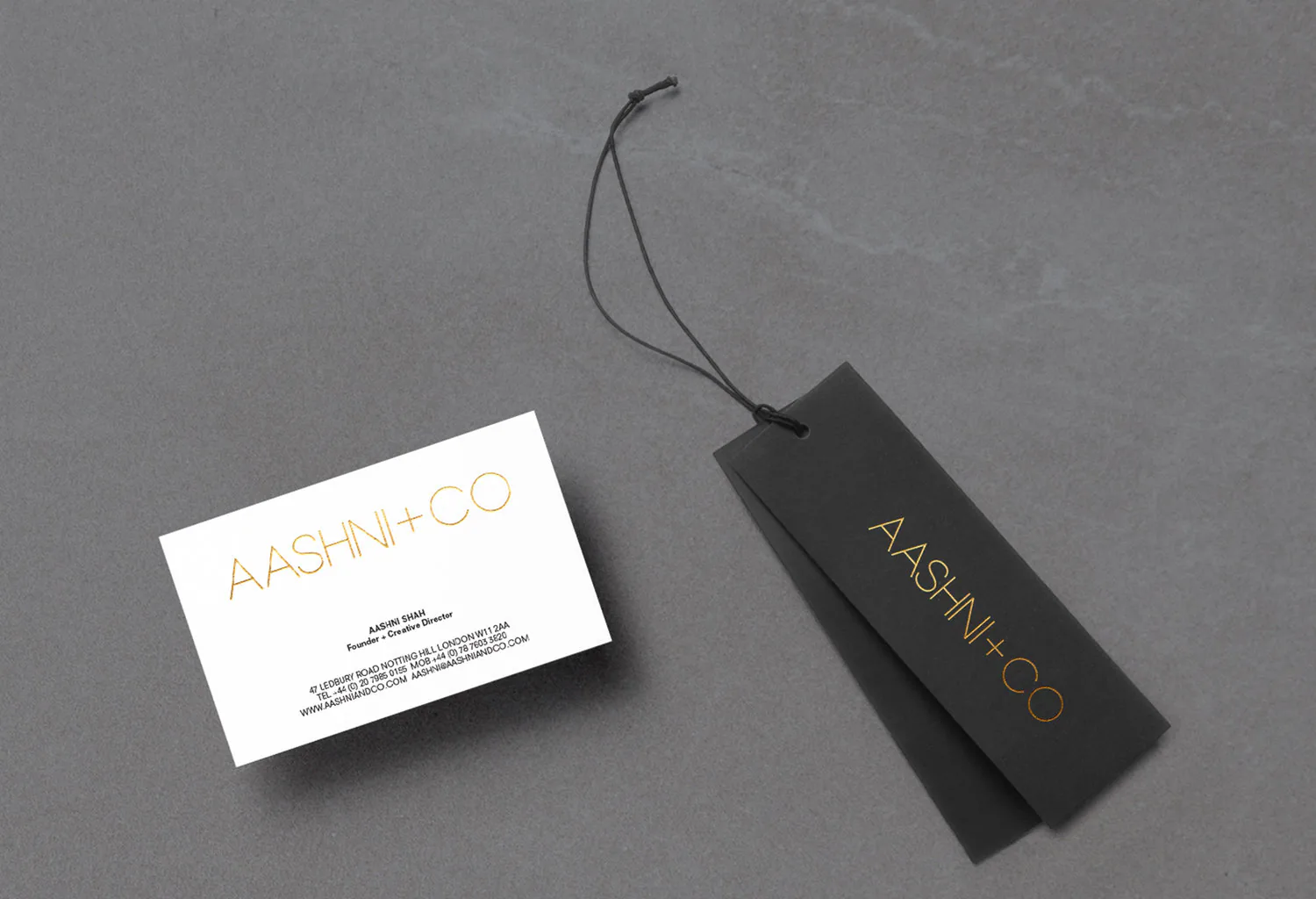 An AASHNI+CO business card beside a black swing tag on a cord.