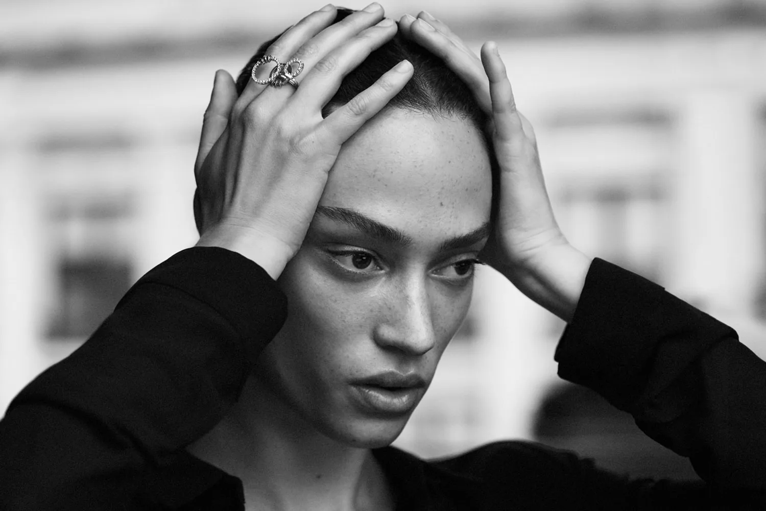 A model wearing rings, hands raised to her hair, in black and white.