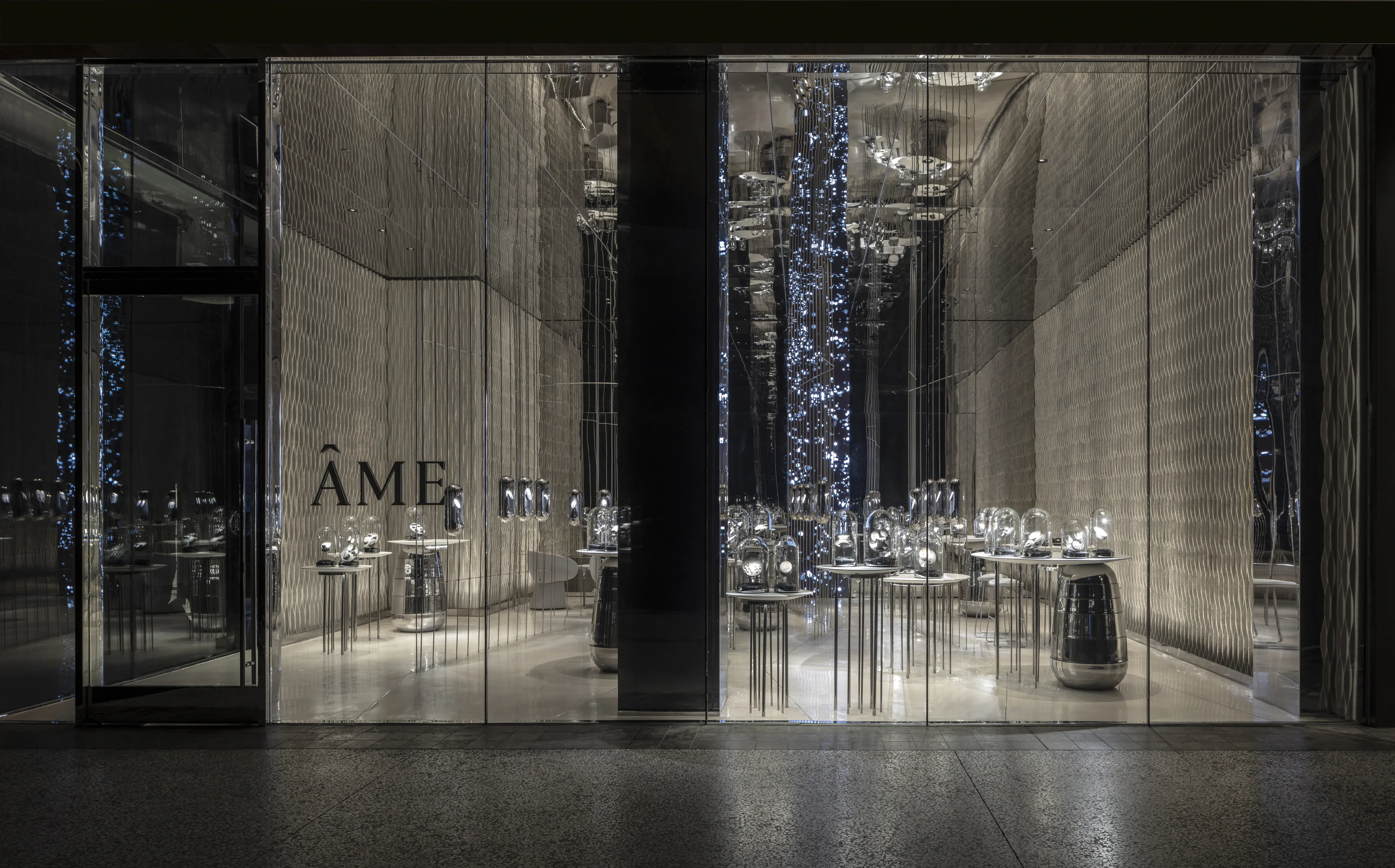 The Ame storefront at night, lit behind a glass facade.