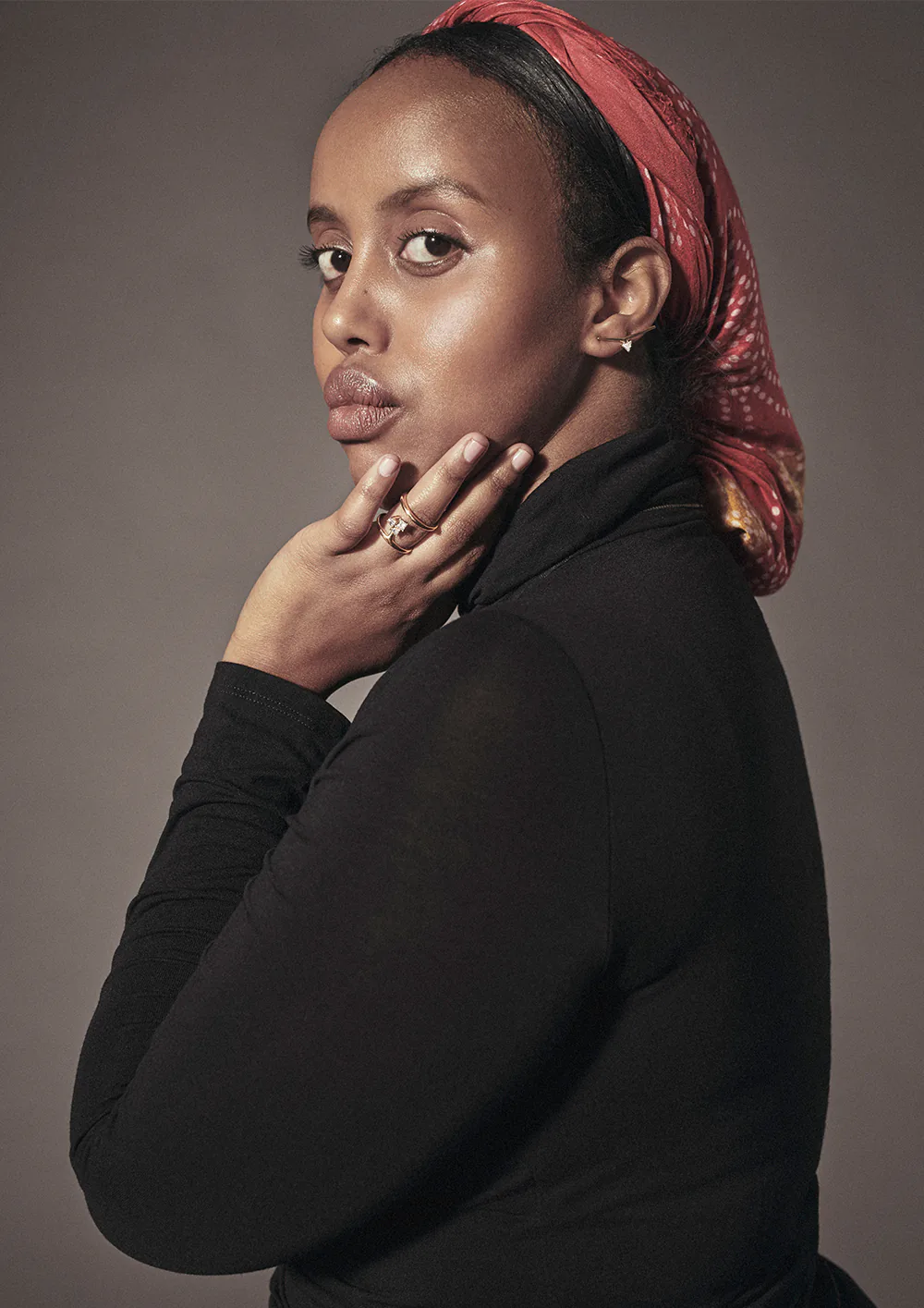 A model in a red headwrap and black polo neck.