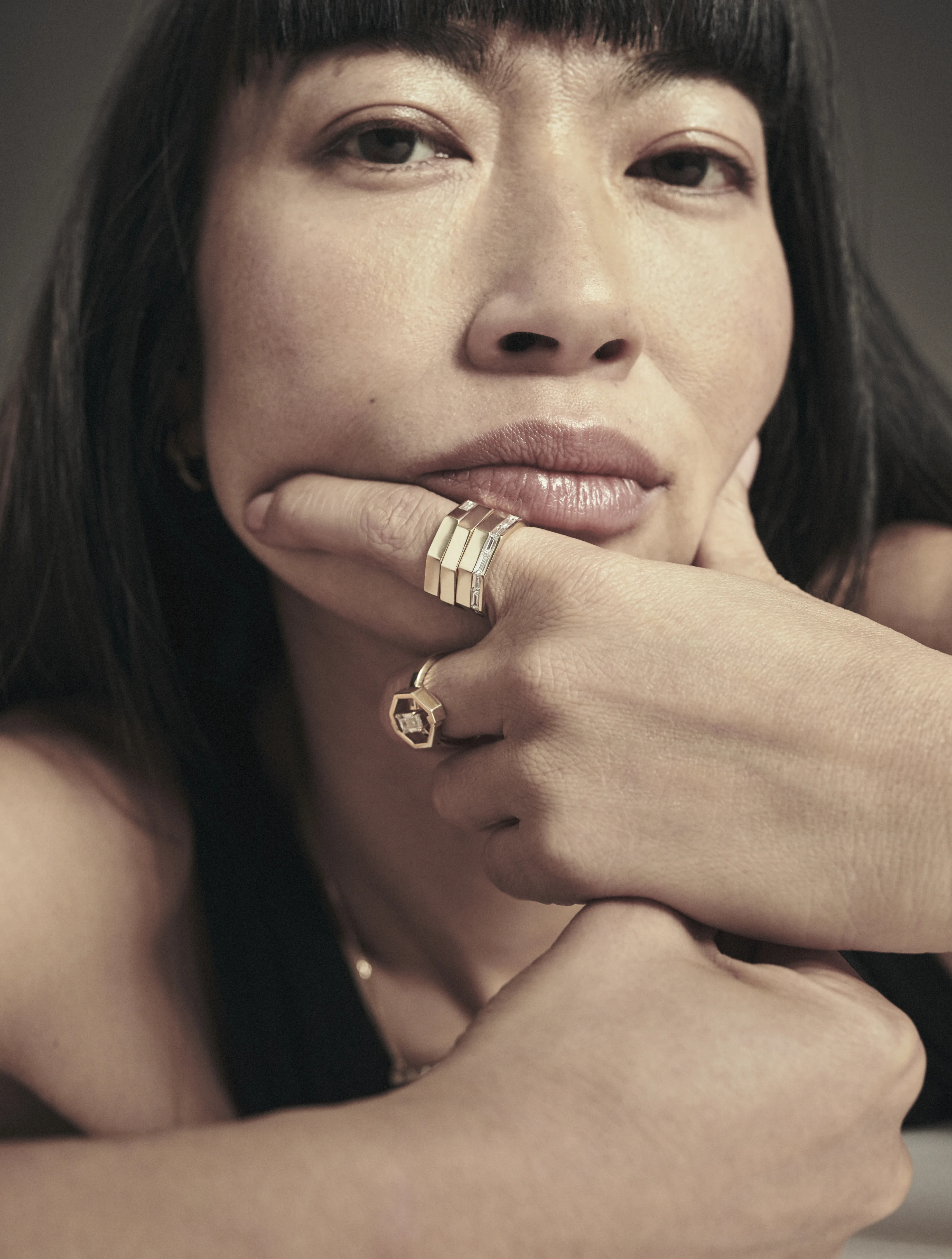 A model resting her chin on her hand, wearing stacked rings.