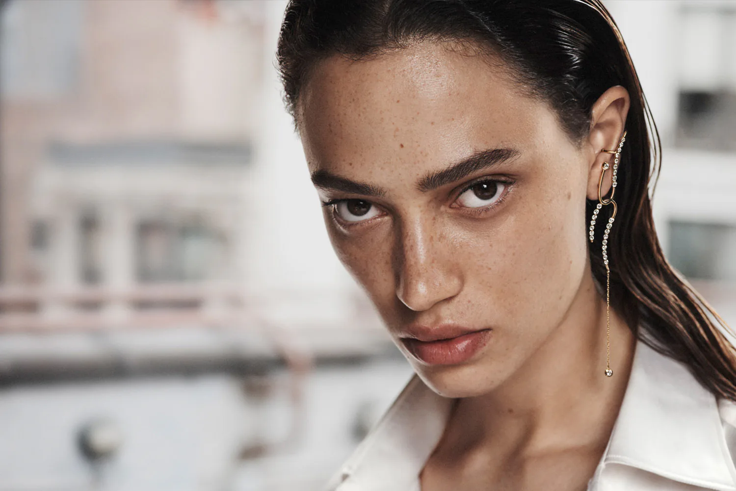A model wearing a drop earring, photographed on a rooftop.