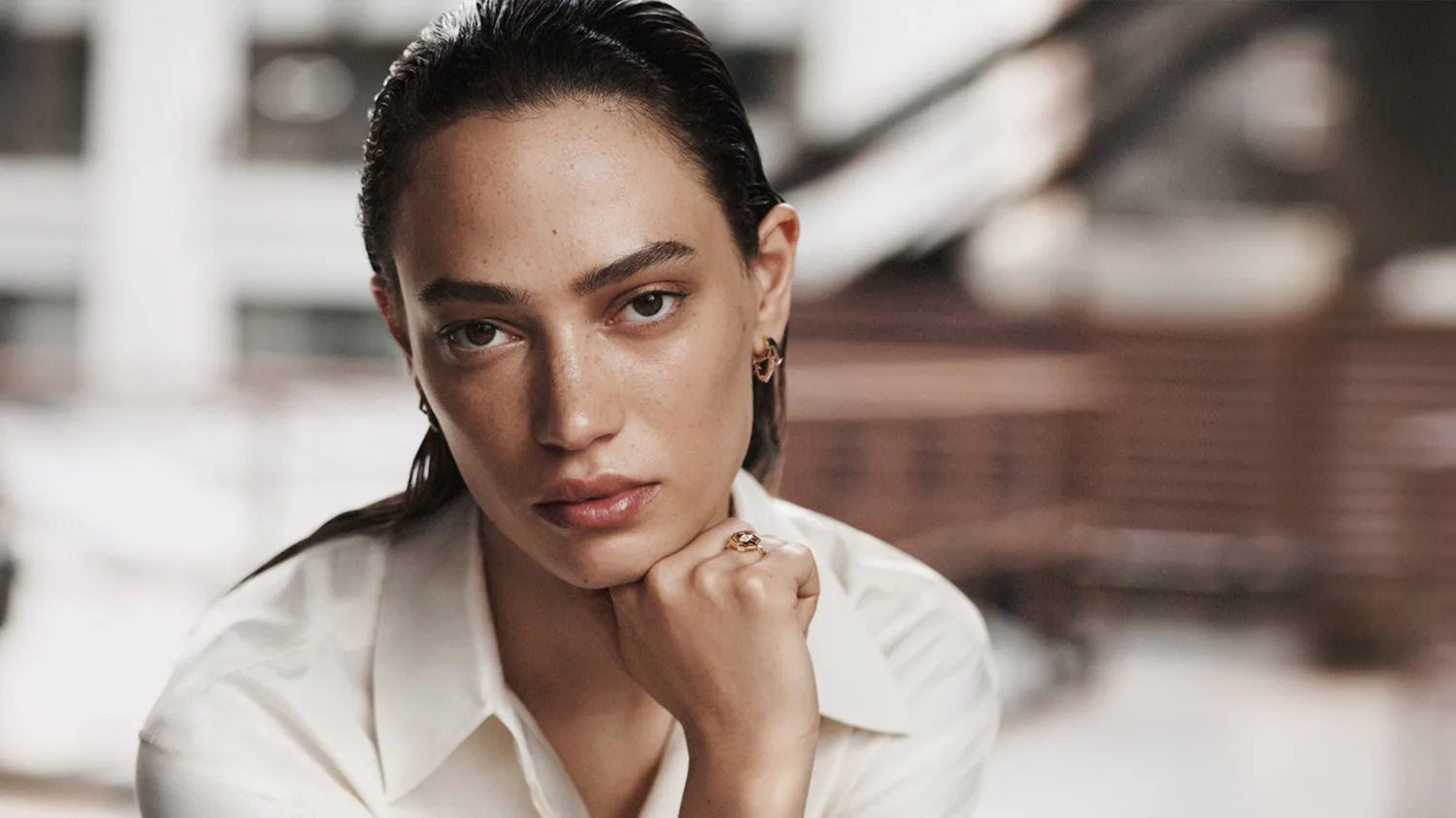 A woman in a white shirt resting her chin on her hand, her hair slicked back.
