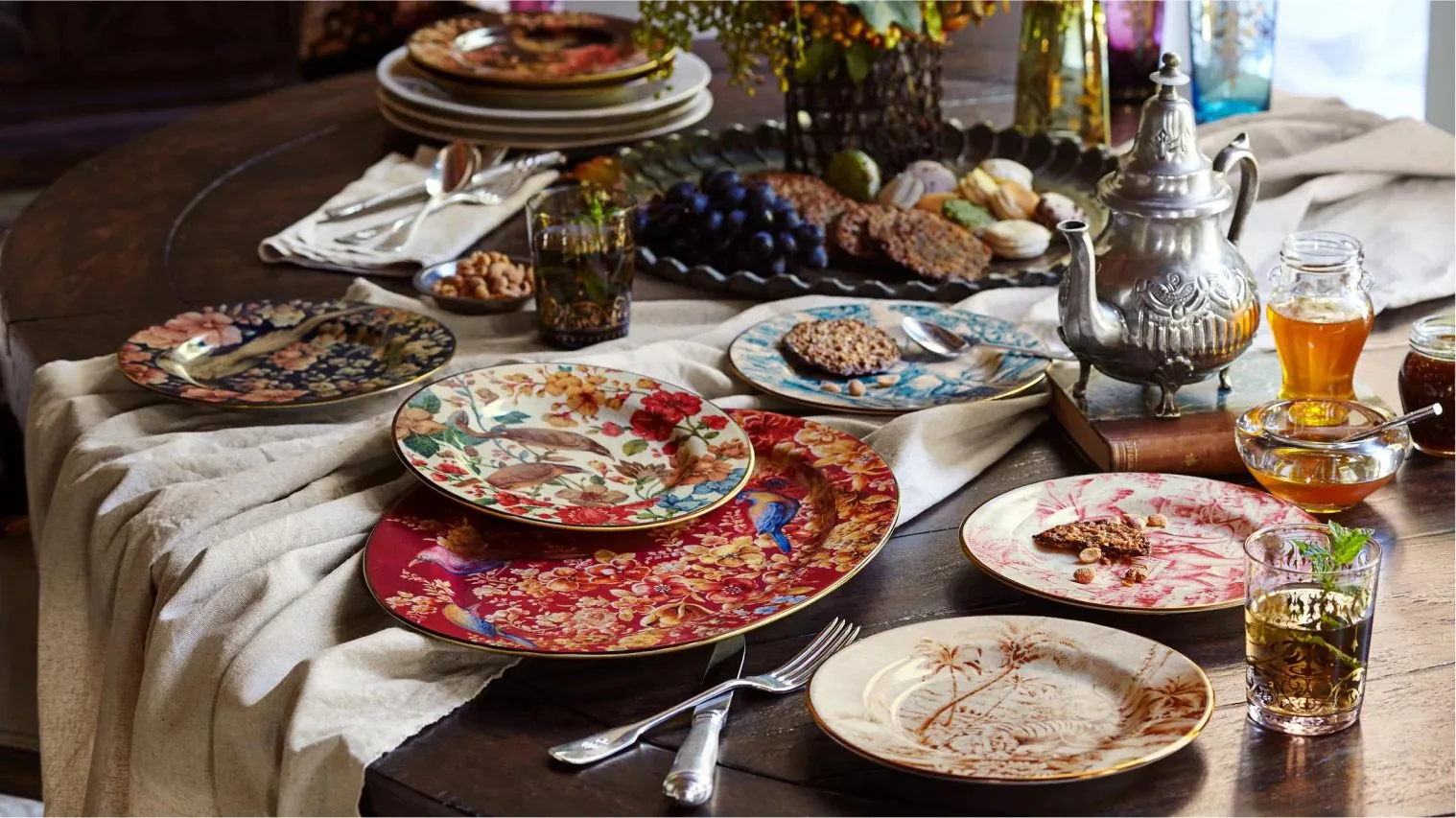 A table laid with patterned plates, pastries and a silver pot of mint tea in gilded glasses.