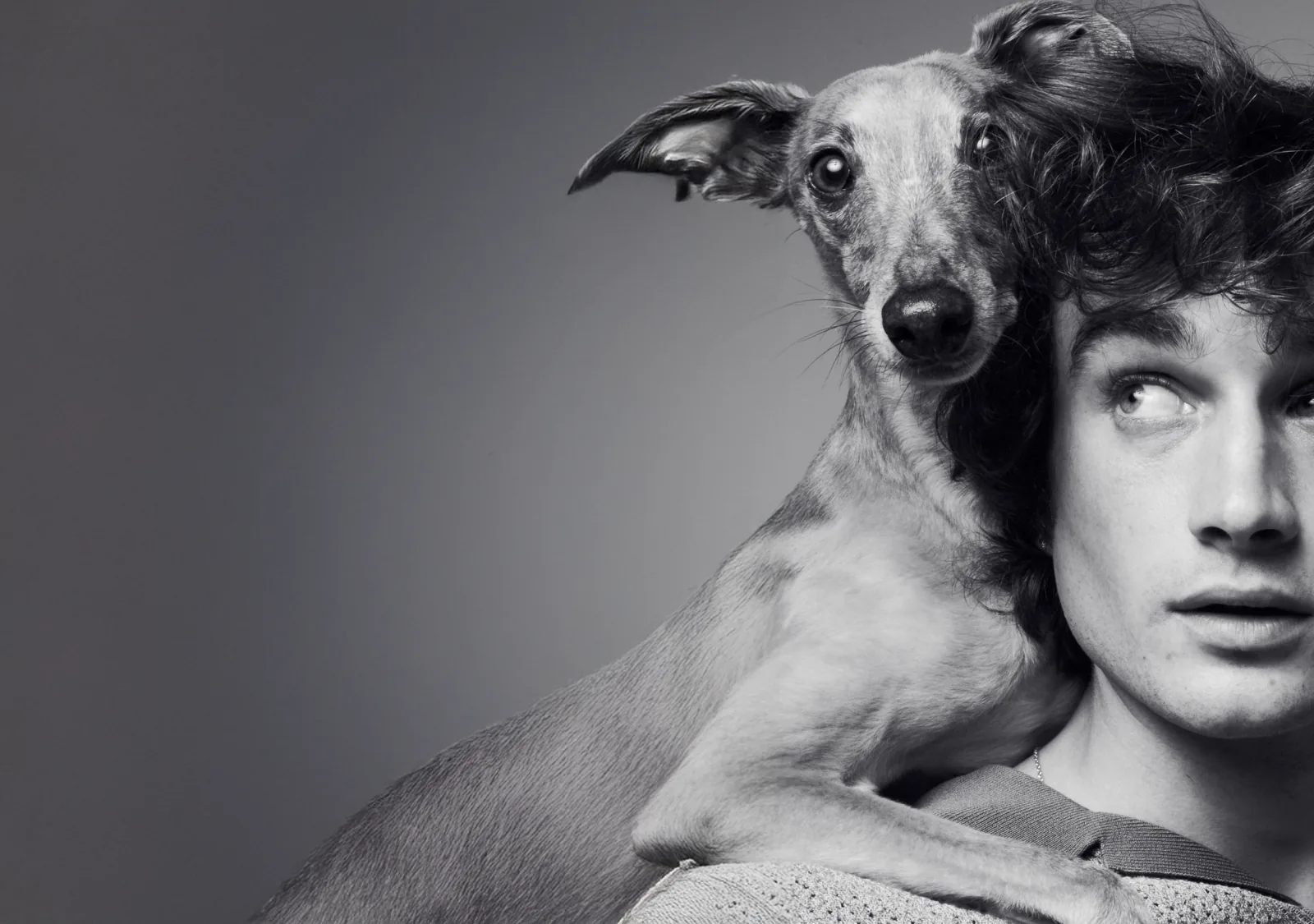 A whippet and a young man cheek to cheek, in black and white.