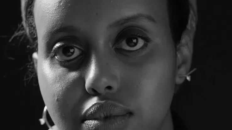 A close portrait of a woman's face in black and white, lit from one side.