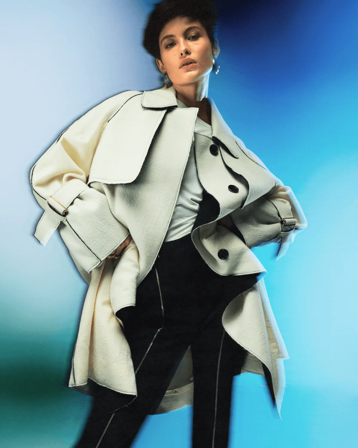 A model in a cream trench coat against a blue gradient ground.