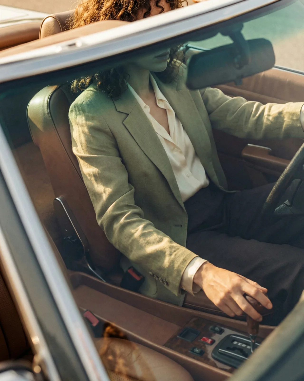 A woman in a pale green jacket at the wheel of a vintage convertible.