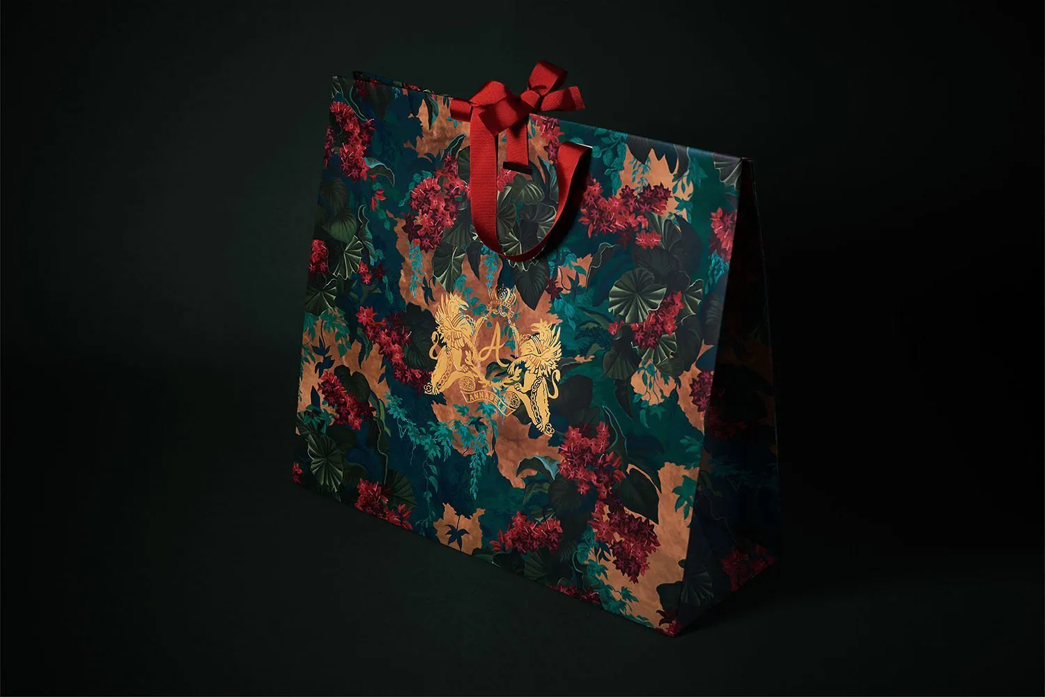 A gift bag printed with red and gold flowers on teal, against black.