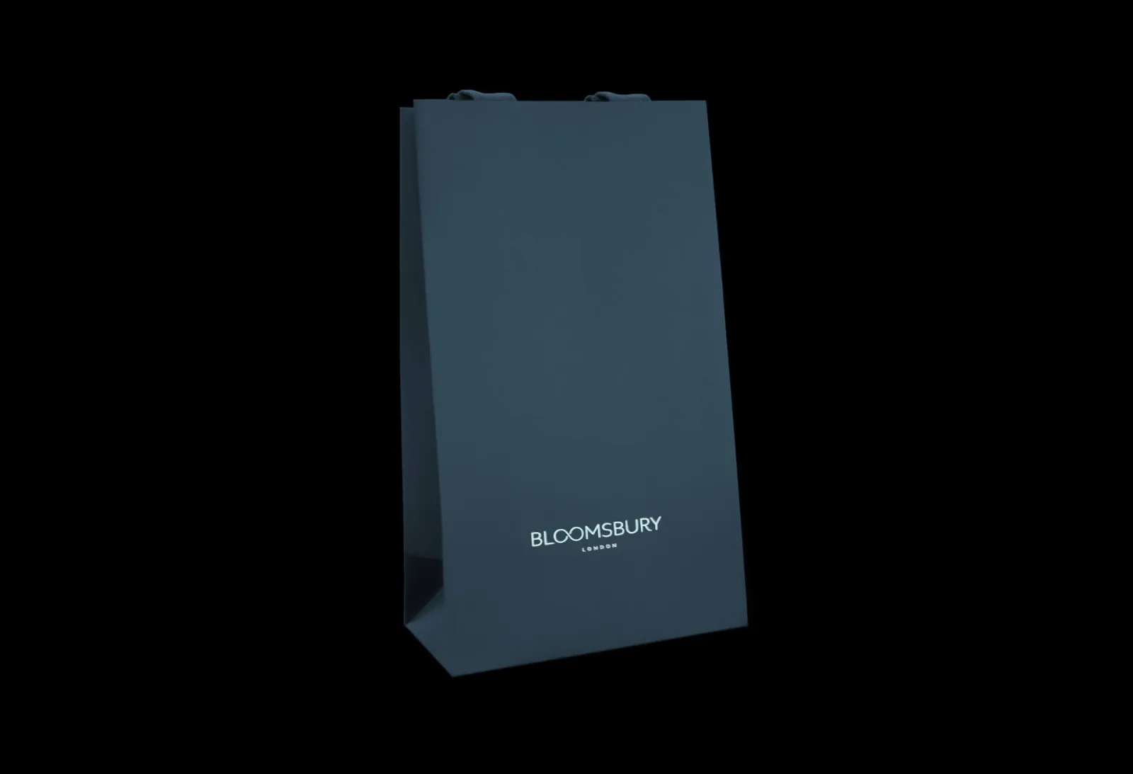 A dark blue Bloomsbury paper bag standing against black.