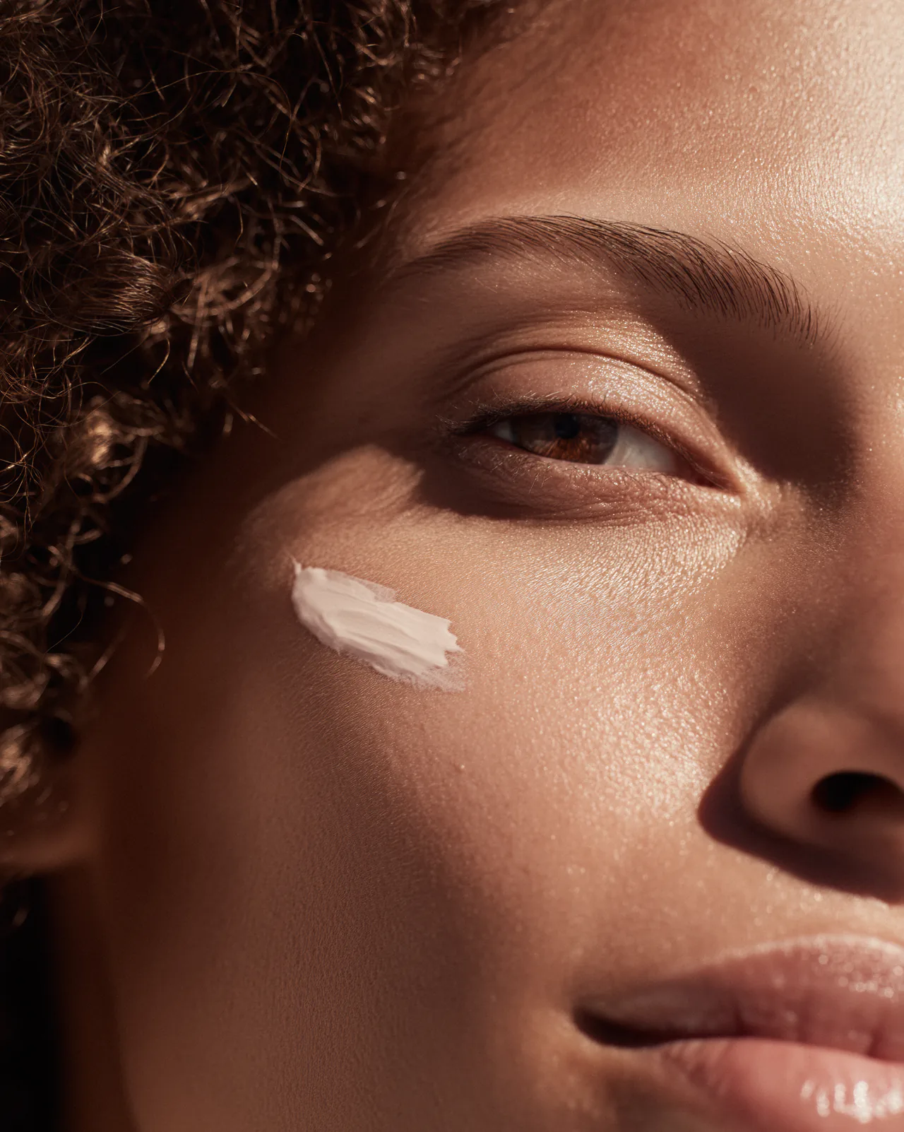 A close view of a woman's eye and cheek, a stroke of white cream on the skin.