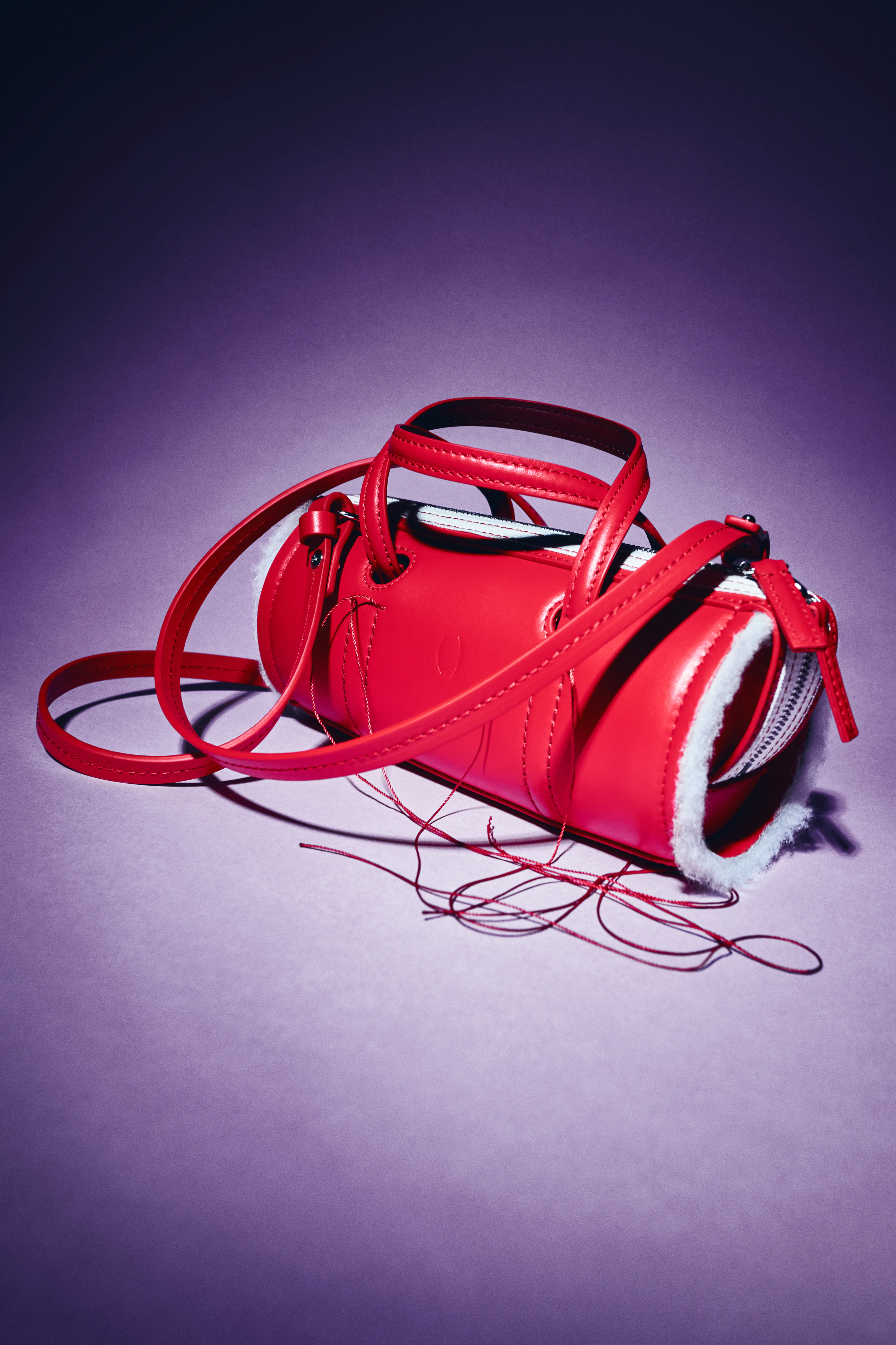 A red patent mini bag with looping straps and cords, on purple.