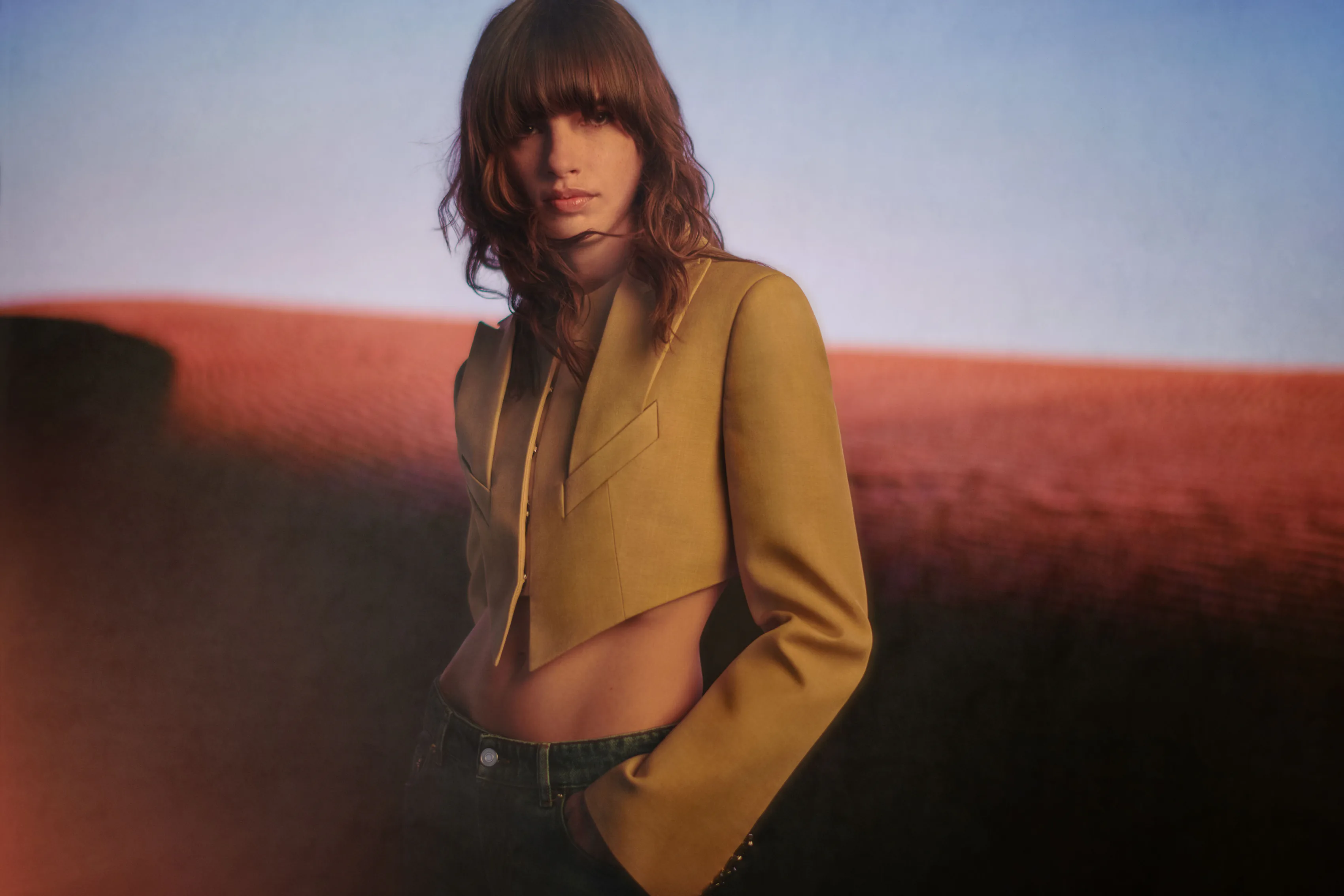 A model in a mustard jacket, photographed on red dunes.