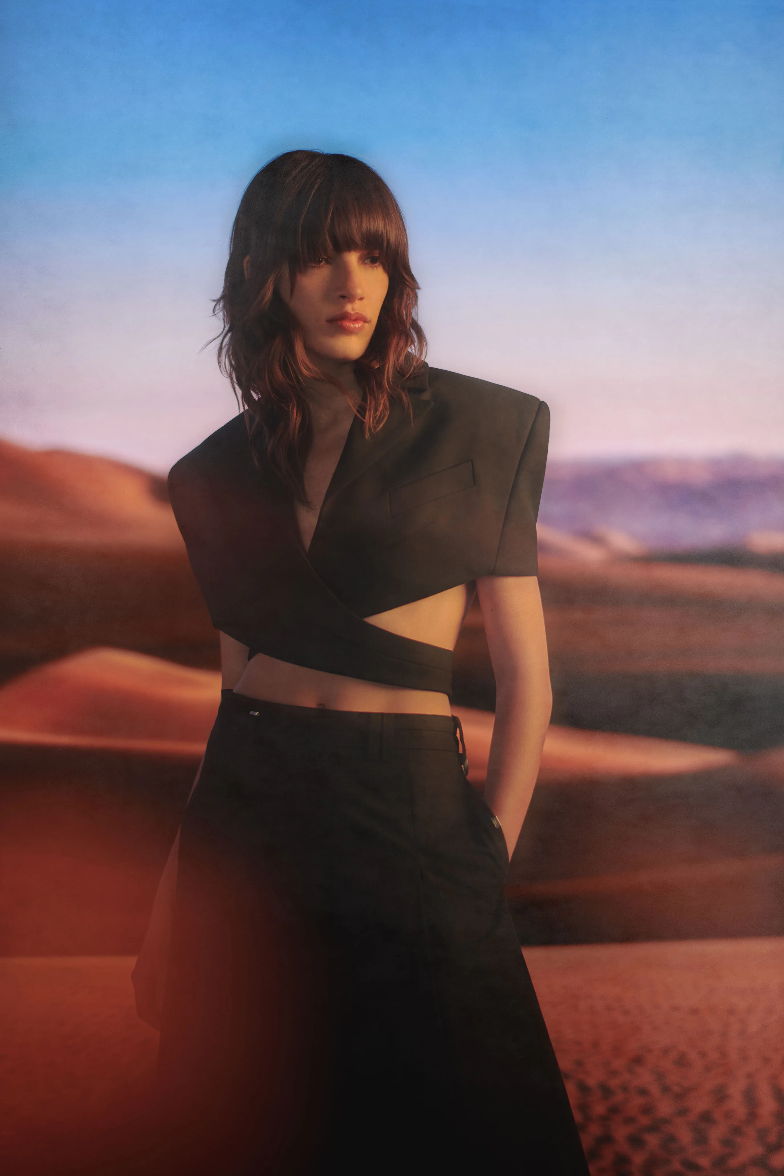 A model in black on a dune at dusk.