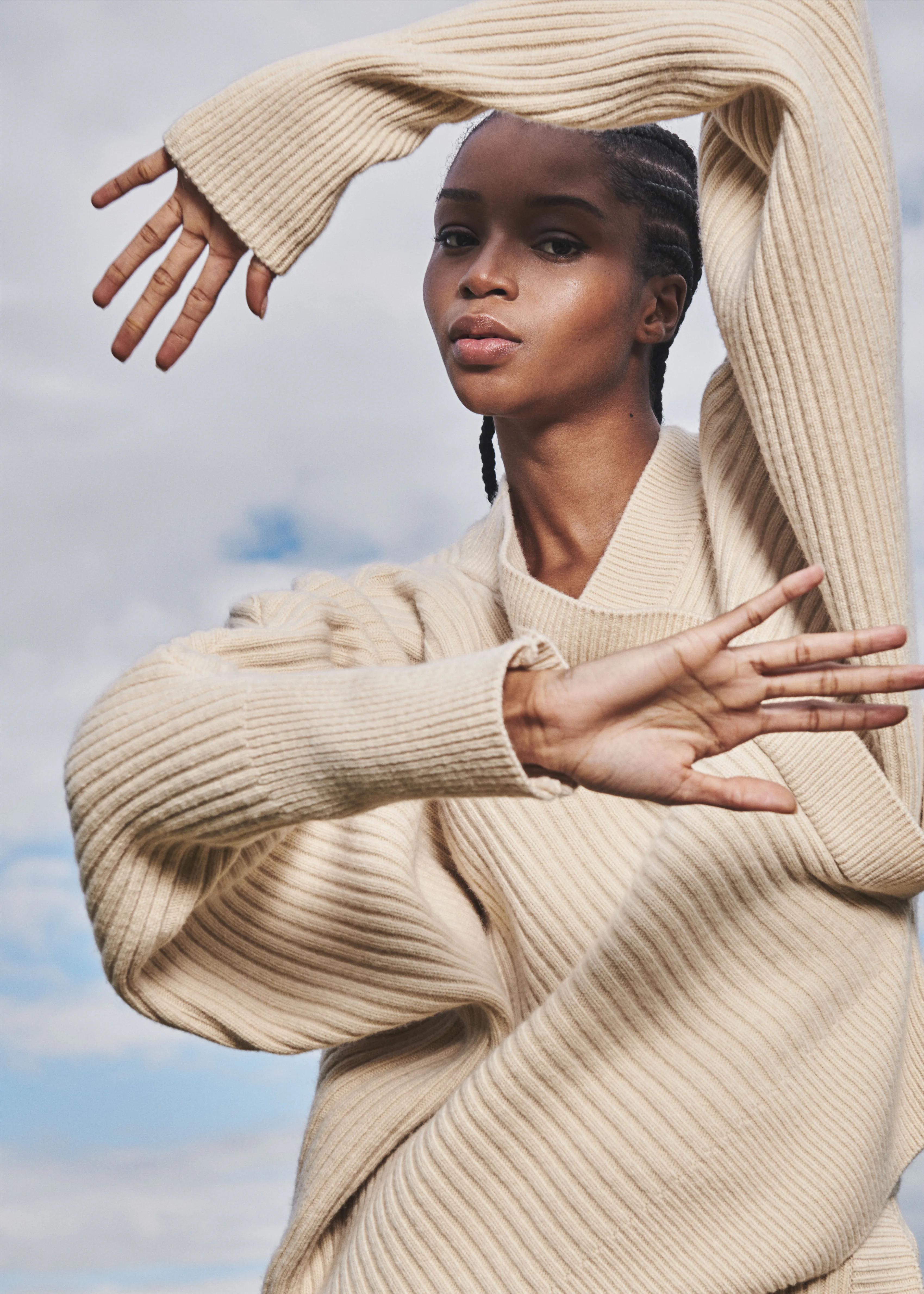 A model in a cream knit, arms raised.