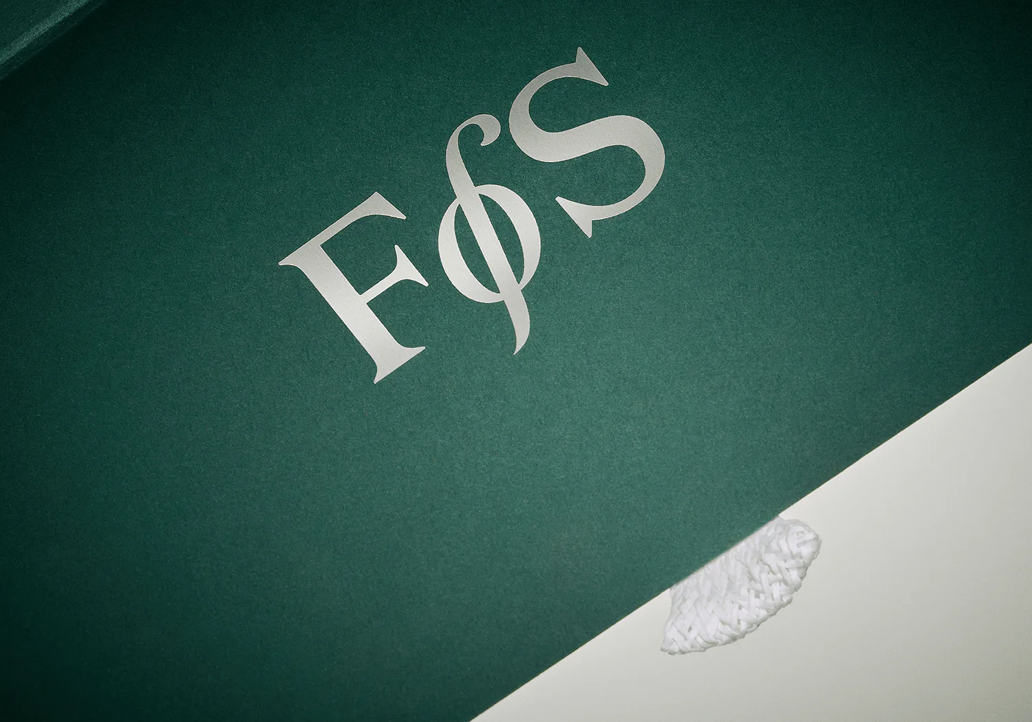 The FoS monogram embossed on green board.