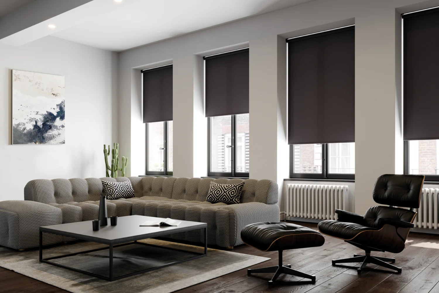 A living room with three windows in dark roller blinds, above a low sofa and lounge chair.