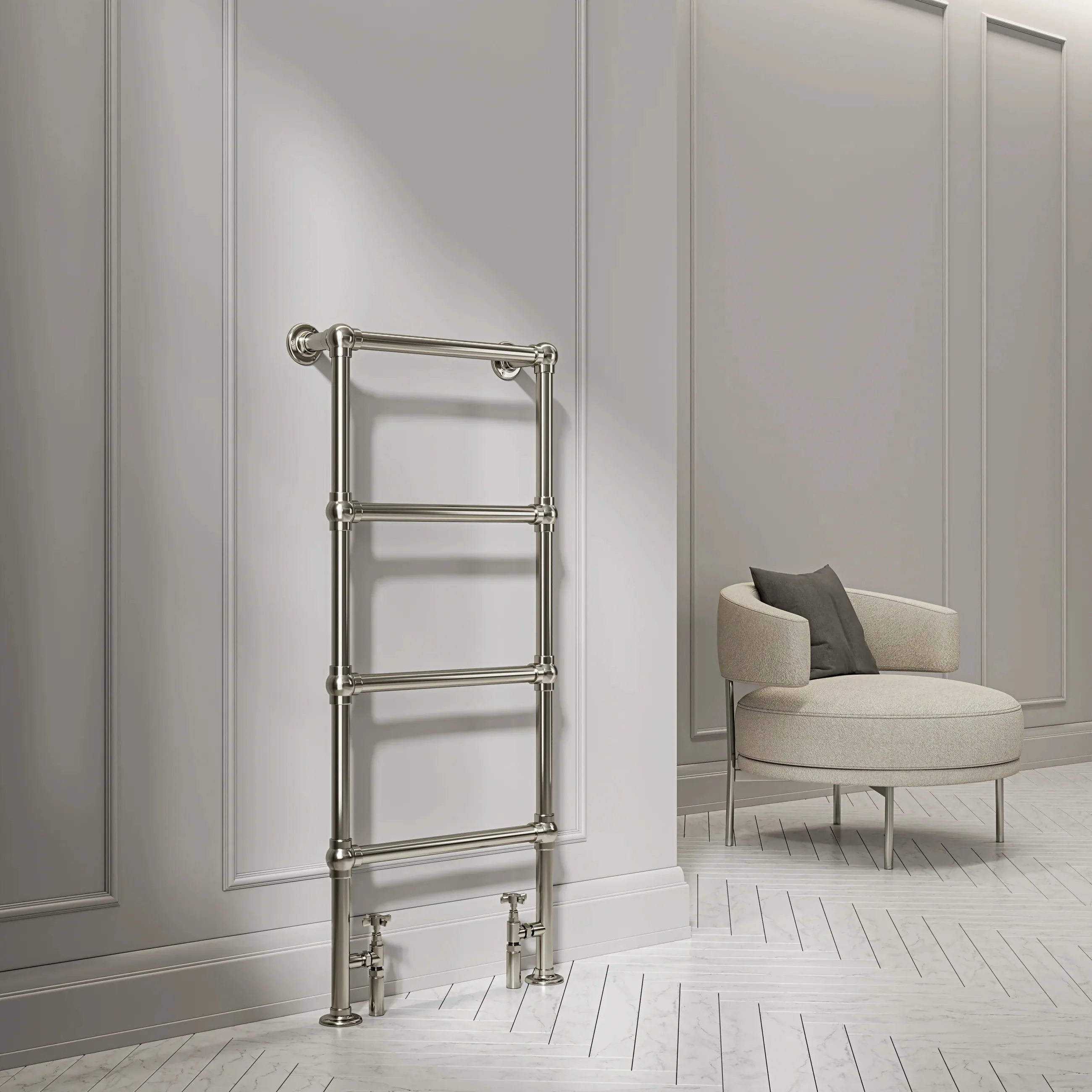 A polished nickel ladder radiator on a panelled wall, an upholstered stool behind.