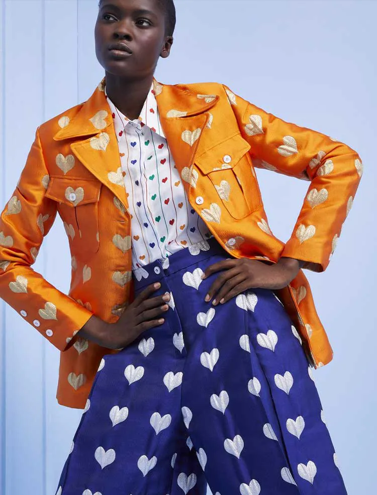 A model in an orange leather jacket over a printed shirt and heart-print trousers.