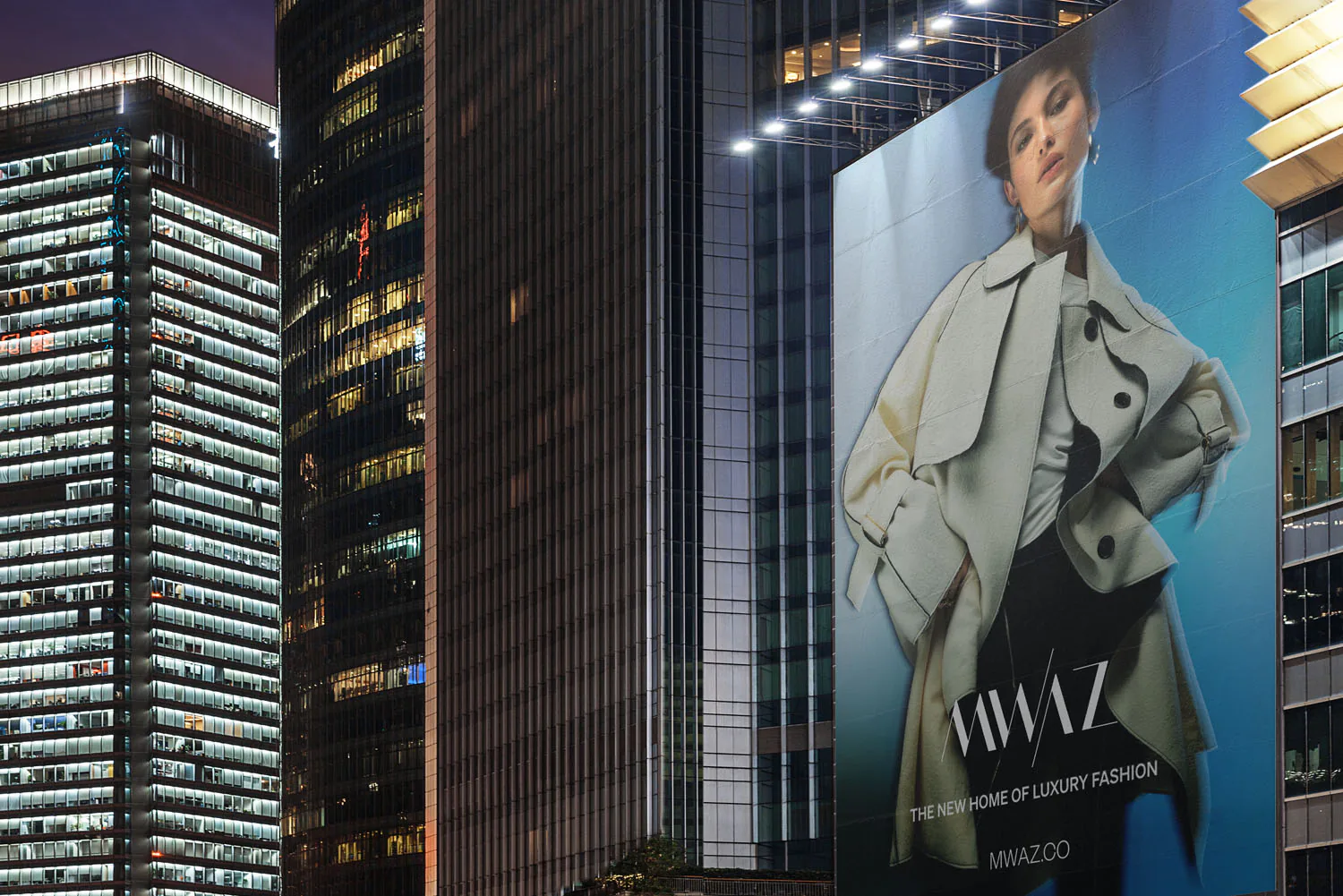 A MWAZ billboard down the side of a tower at night, lit against the city.