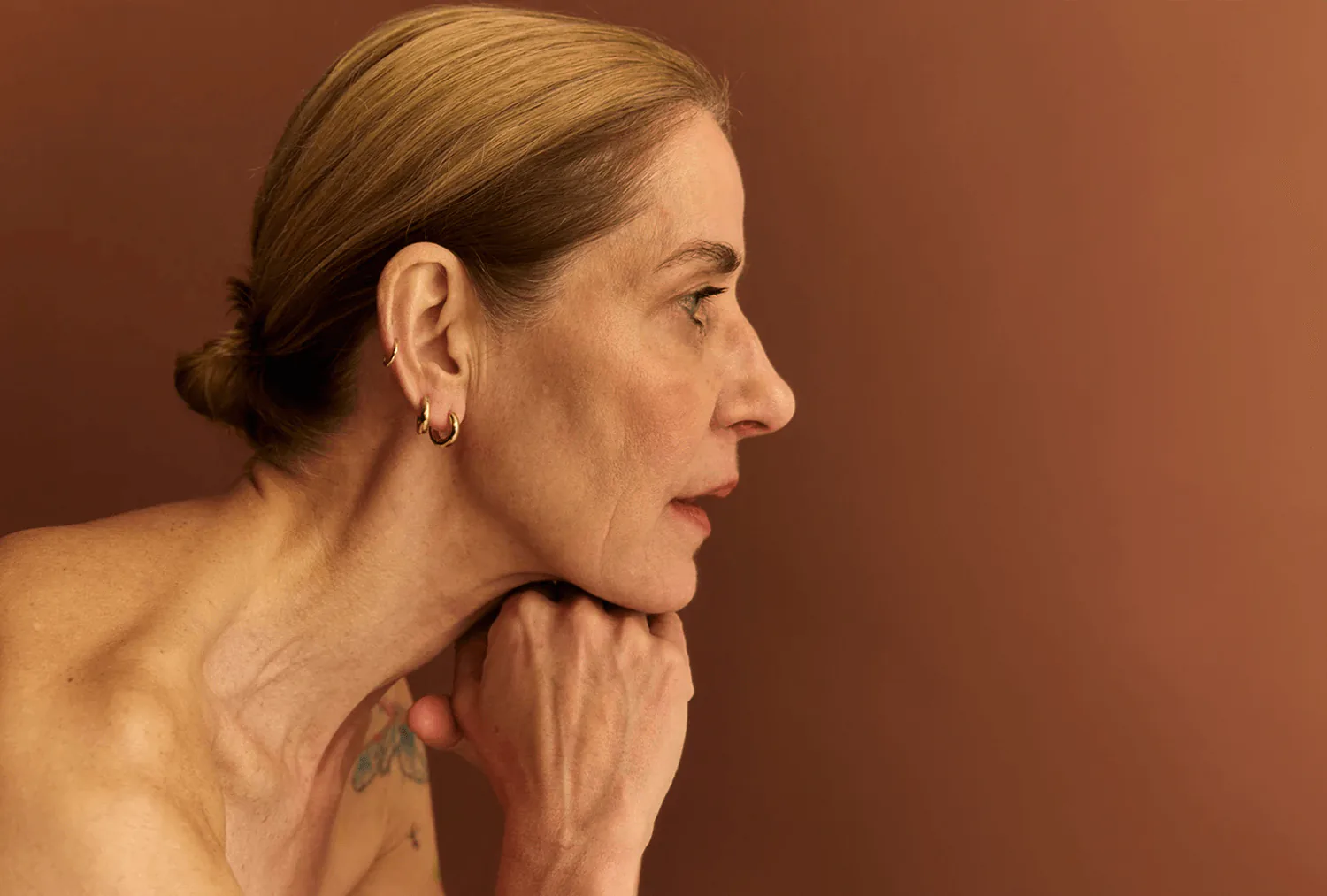 A model in profile against terracotta, wearing a gold hoop.
