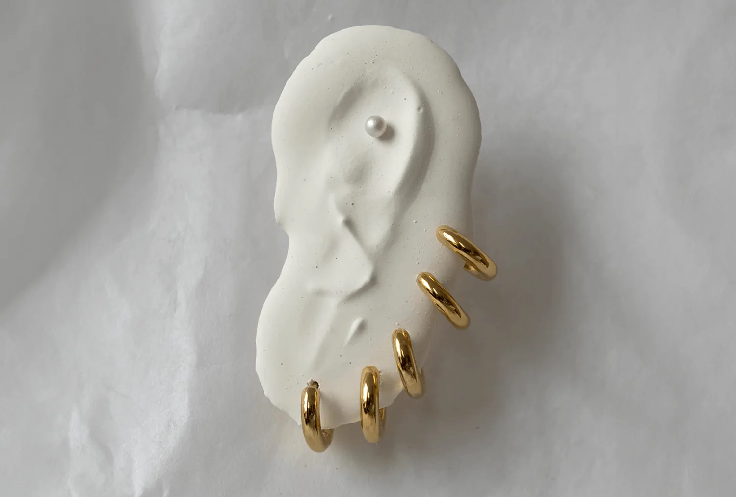A white plaster ear cast set with a row of gold hoops.