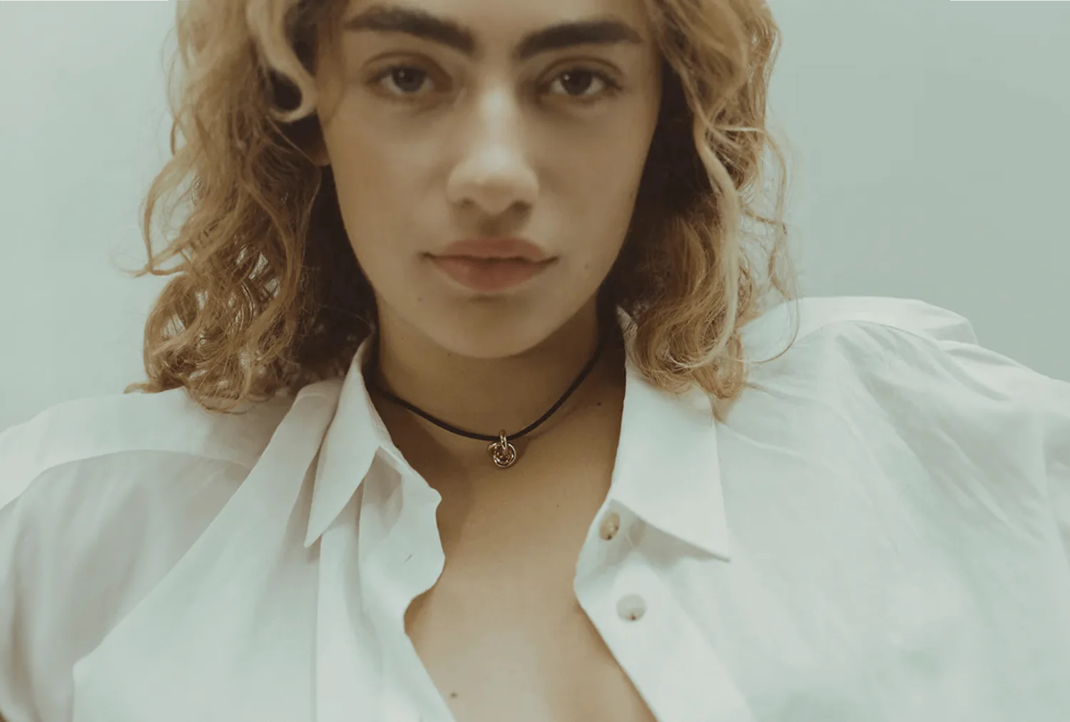 A model in an open white shirt with a fine pendant at her collarbone.