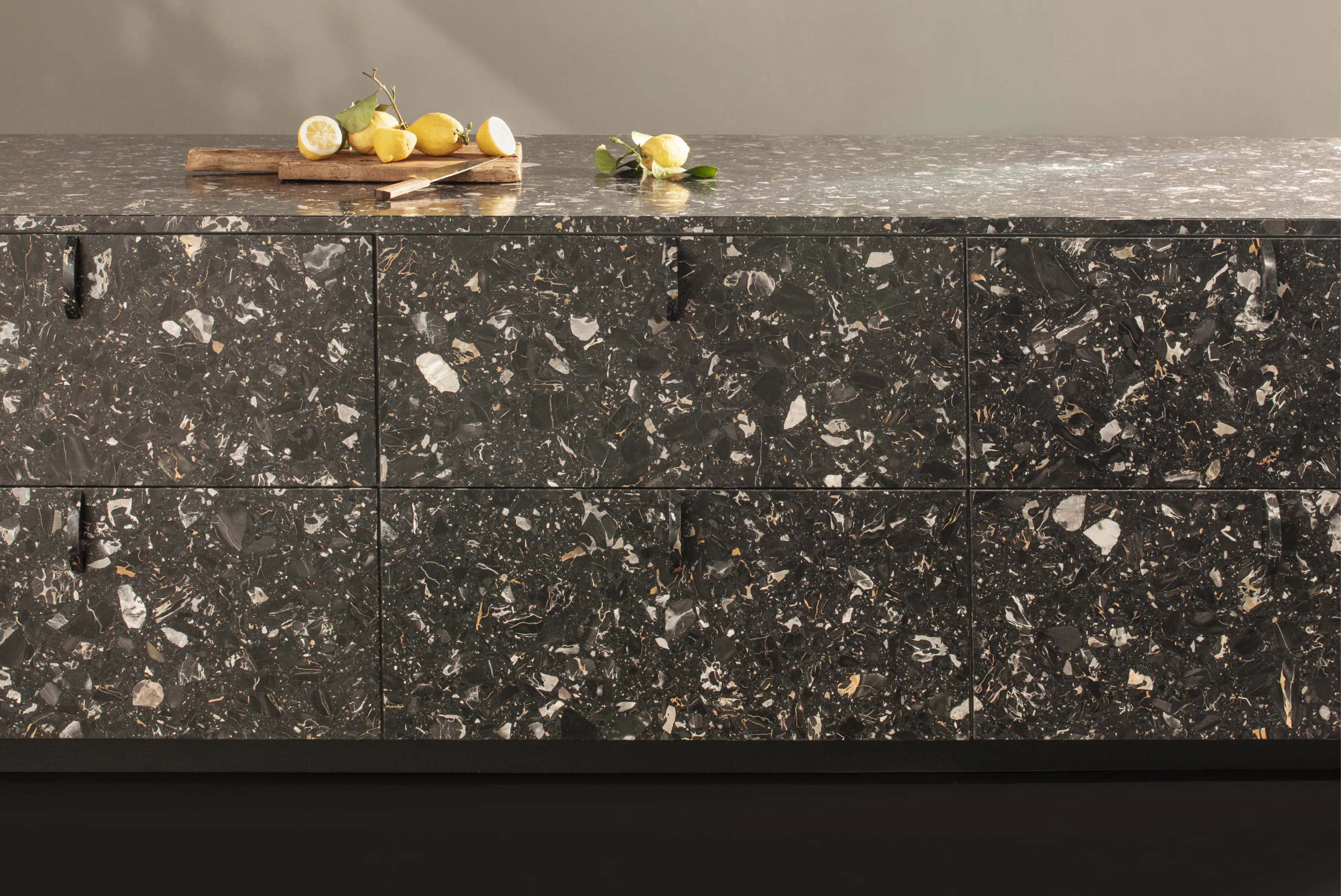 A terrazzo kitchen island in dark stone, with lemons on a wooden board along the top.