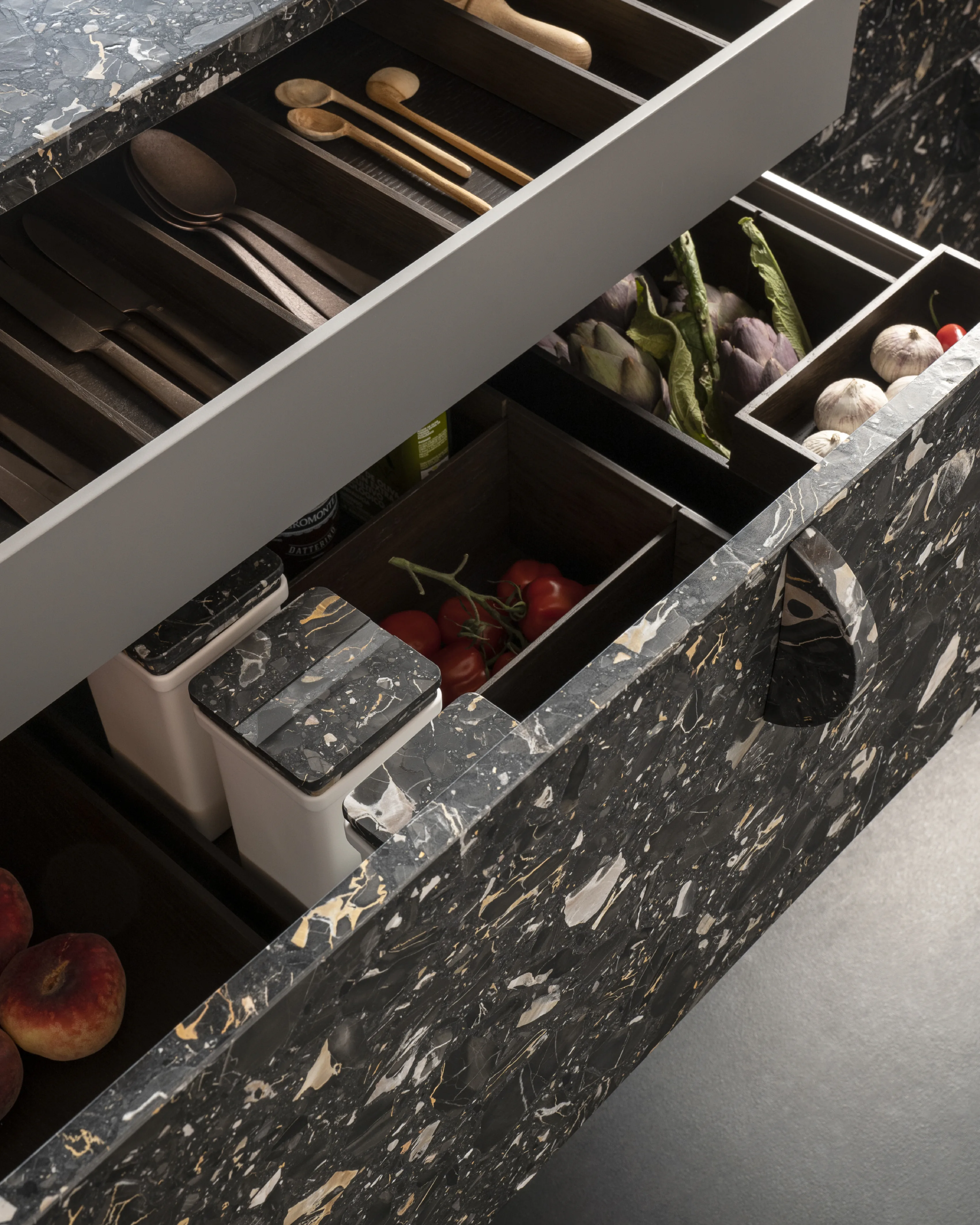 An open cutlery drawer with compartments of utensils, beside a dark marble worktop.