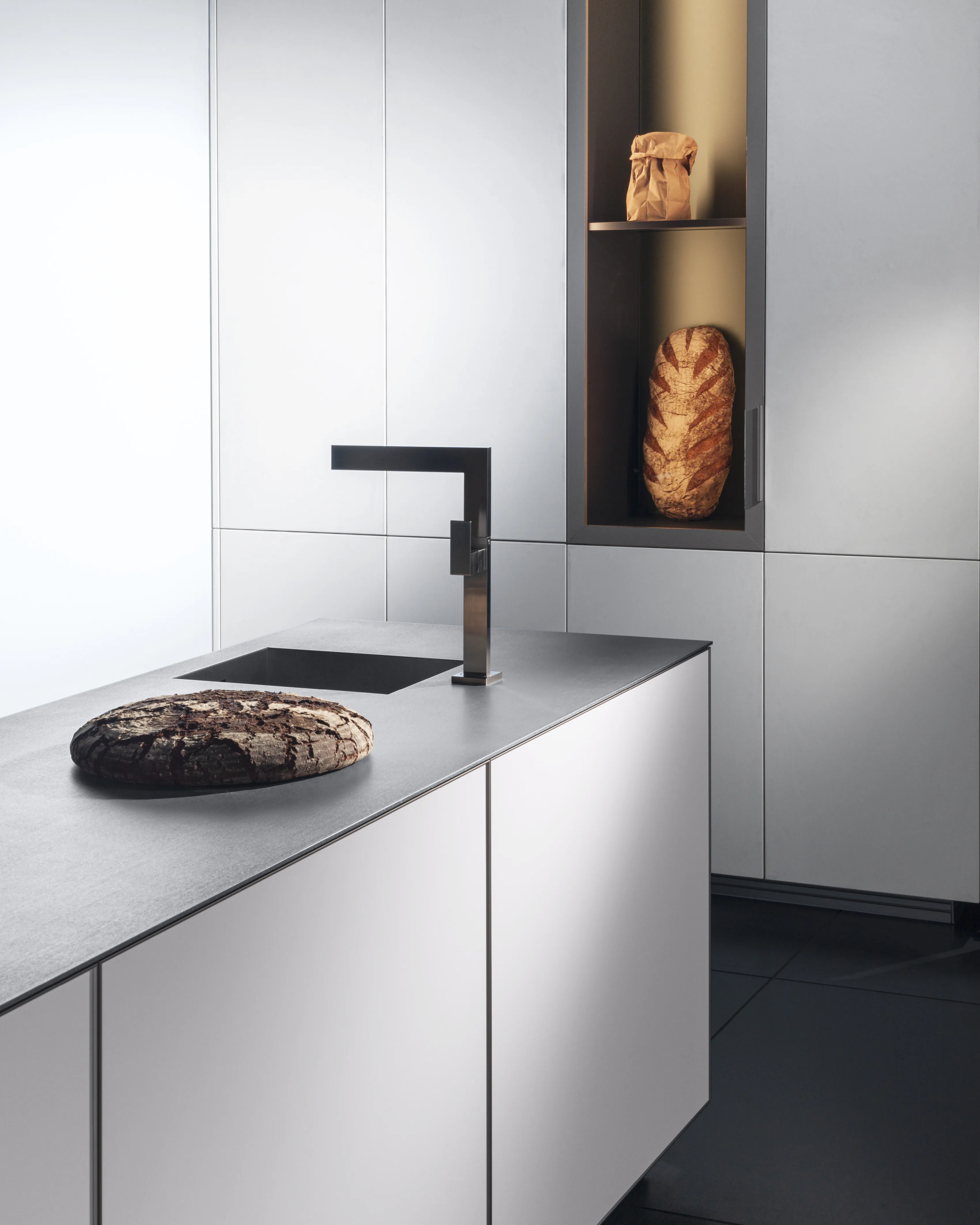 A white kitchen island with a black tap and a round loaf, beside a recessed shelf.