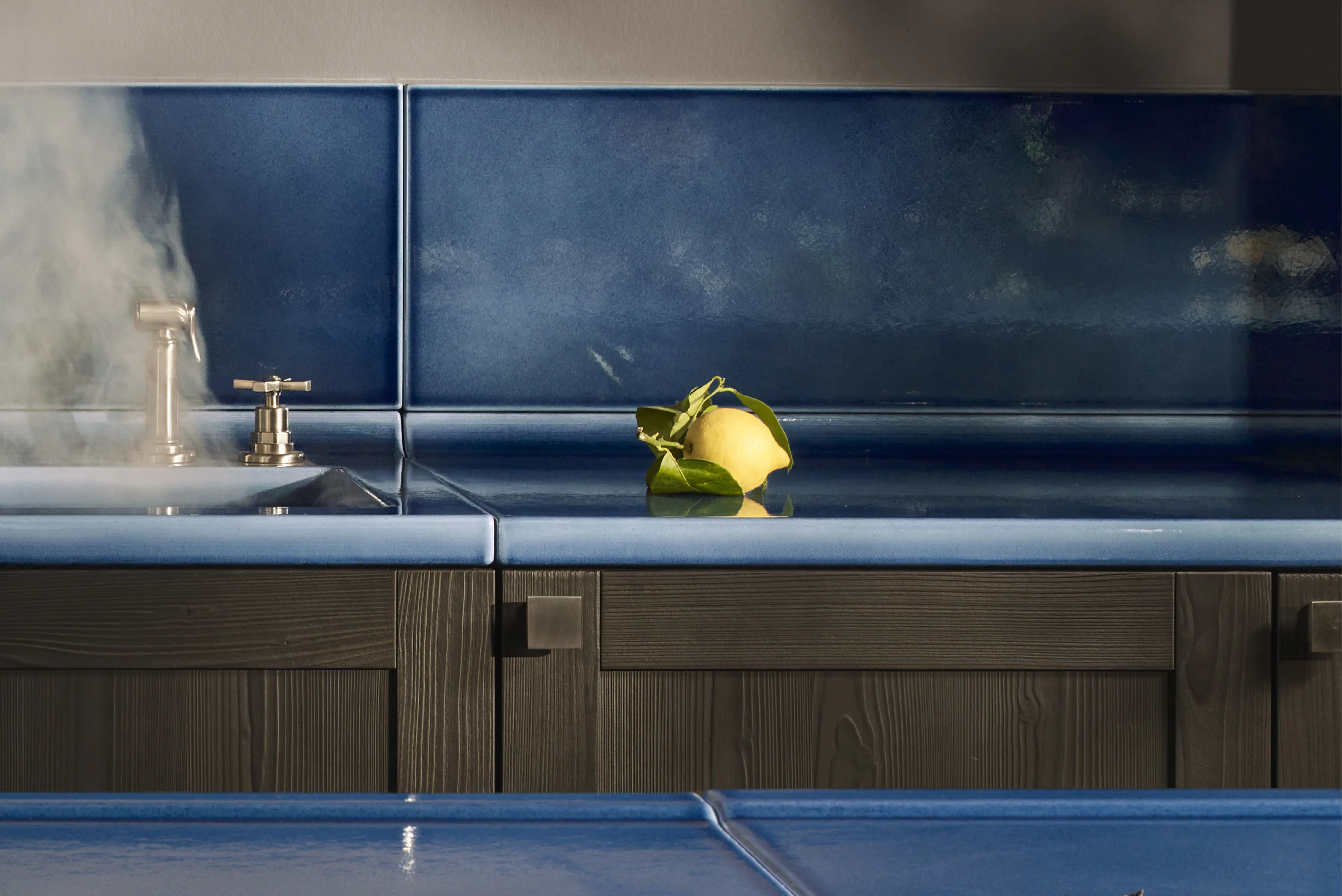 A deep blue splashback behind a brass tap and a sink, with steam rising.
