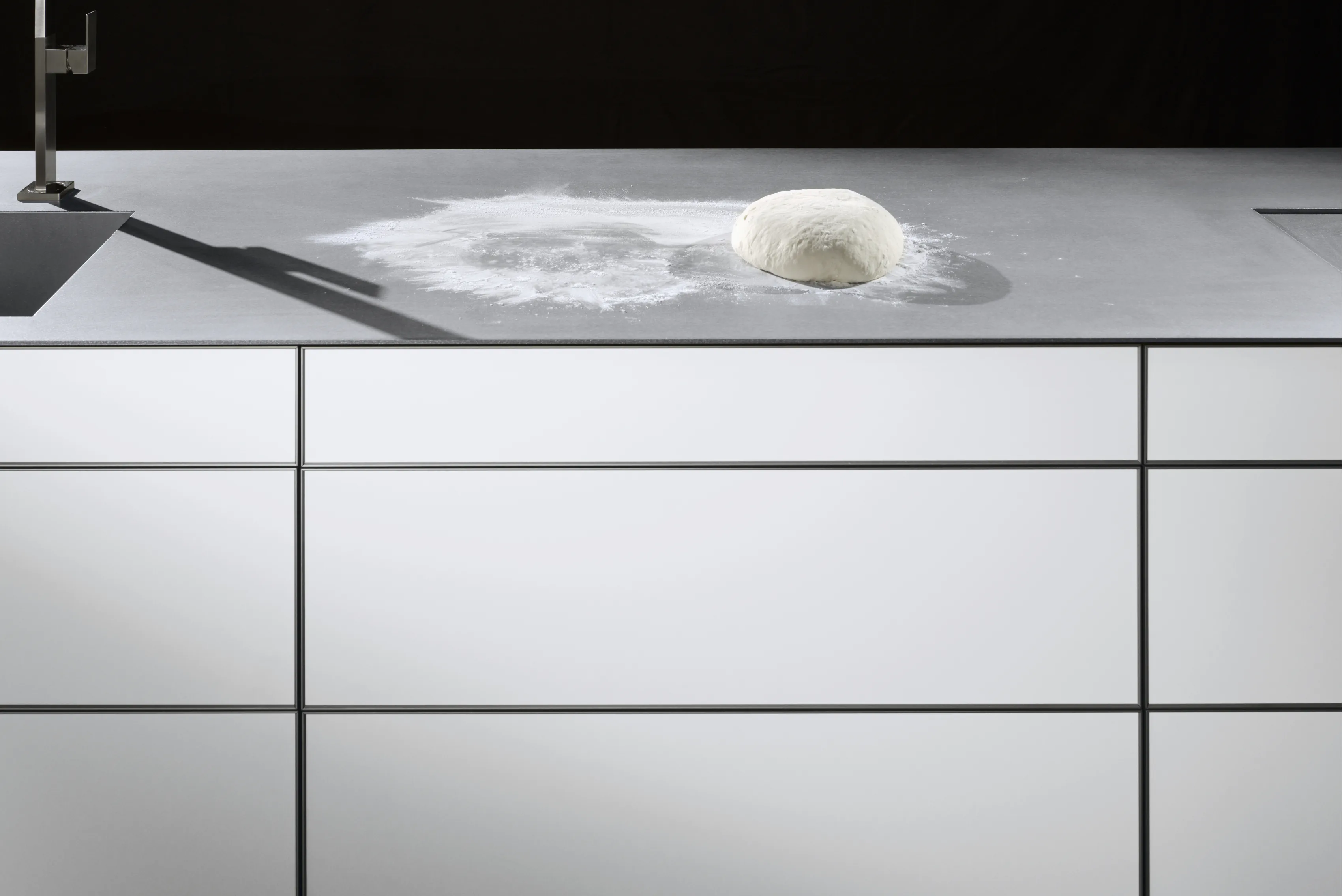Dough resting in scattered flour on a white worktop, lit from one side.
