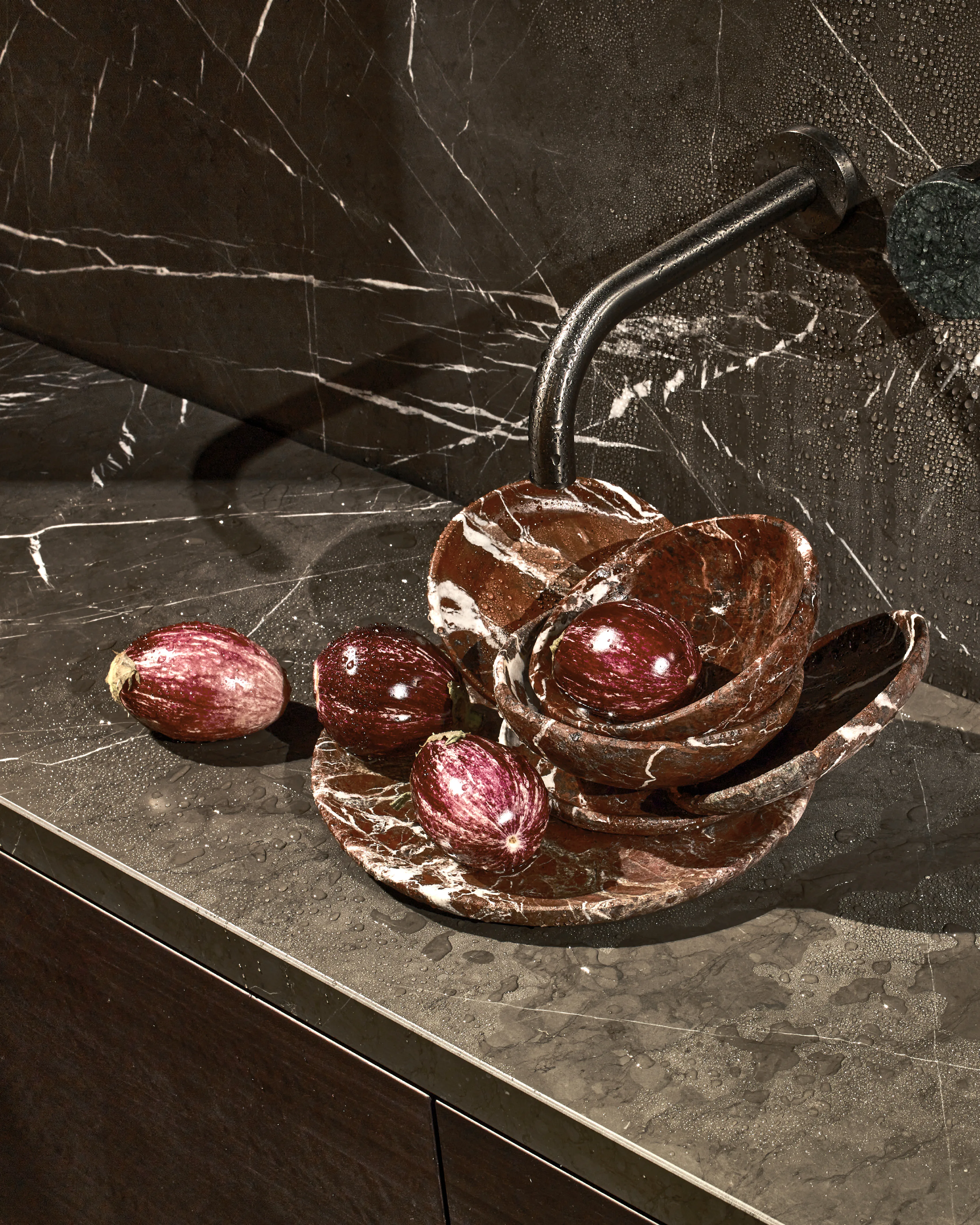 Copper-glazed petal dishes holding figs on veined brown marble, a slim tap above.