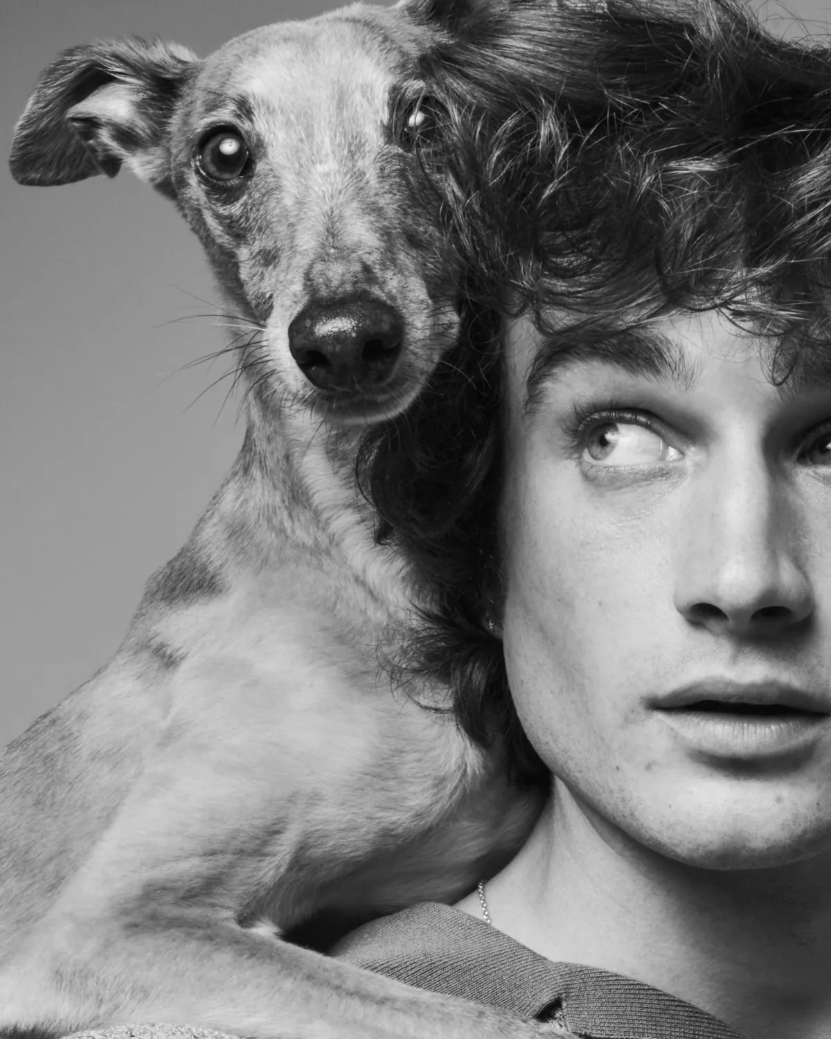 A young man and a spotted dog cheek to cheek, in black and white.