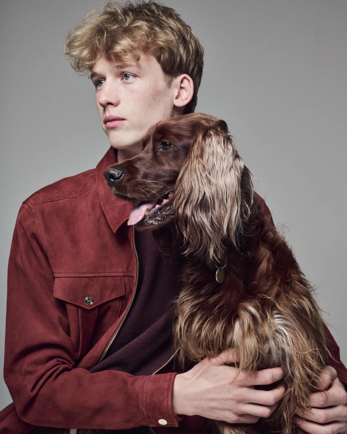 A young man in a rust jacket with a red setter leaning across his chest.