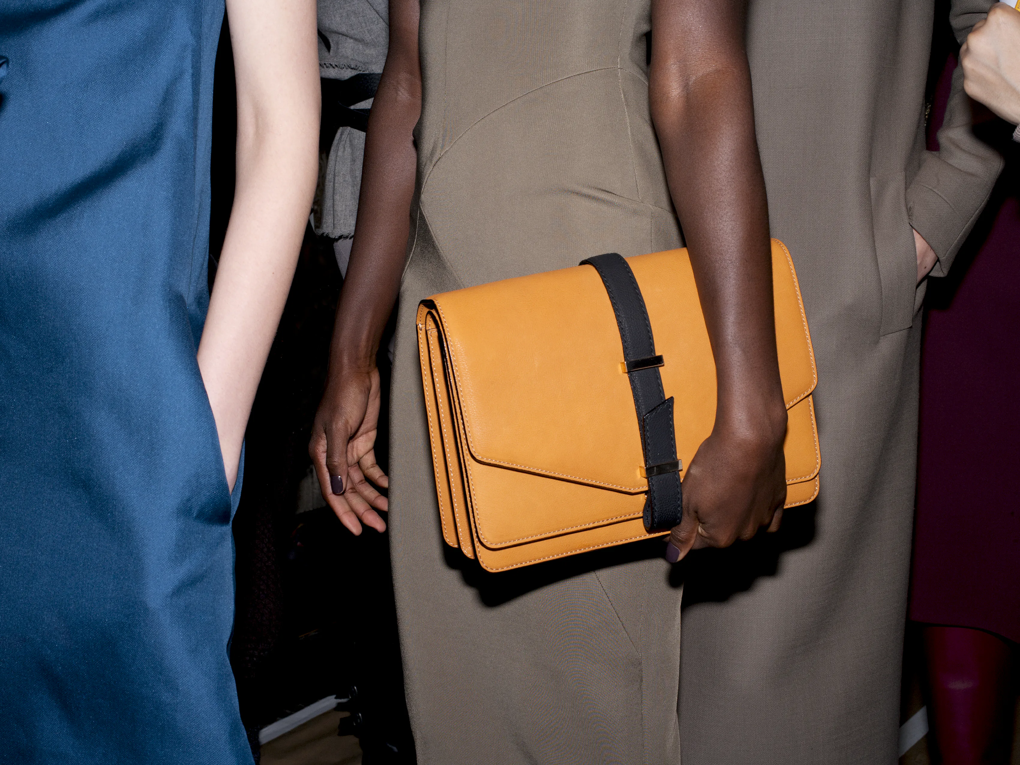 A model carrying an orange clutch bag with a black strap.