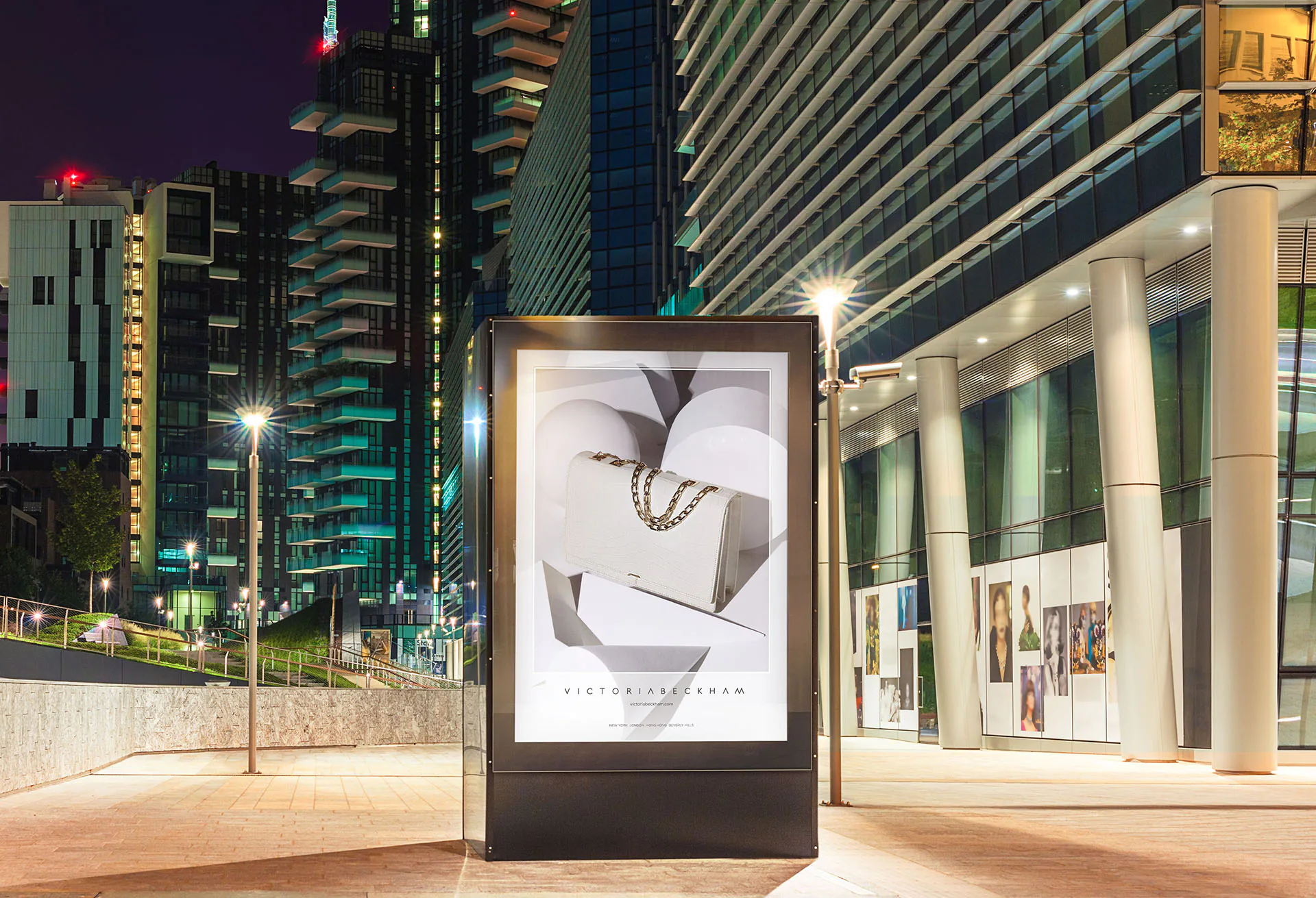 A lit Victoria Beckham billboard on a city street at night.