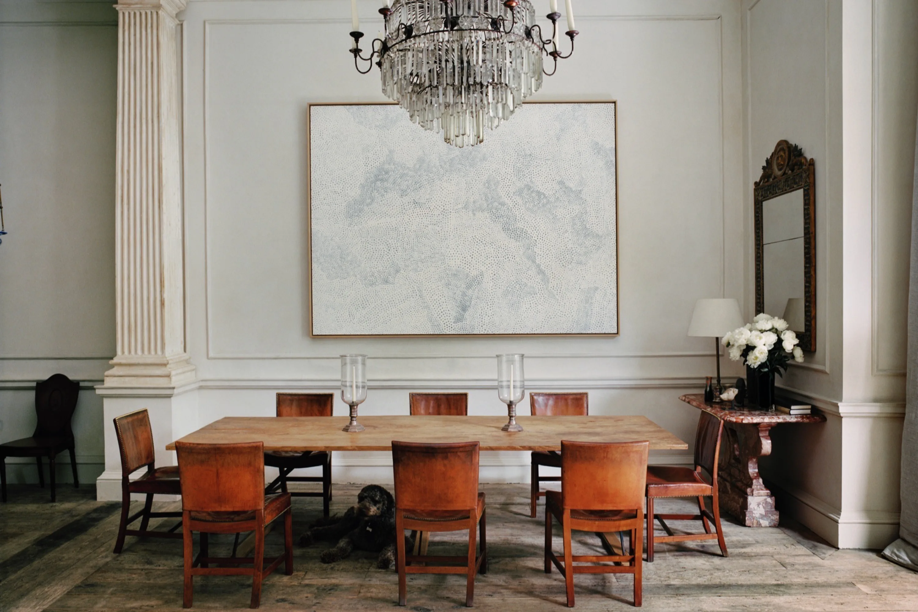 A panelled dining room with tan leather chairs under a chandelier.